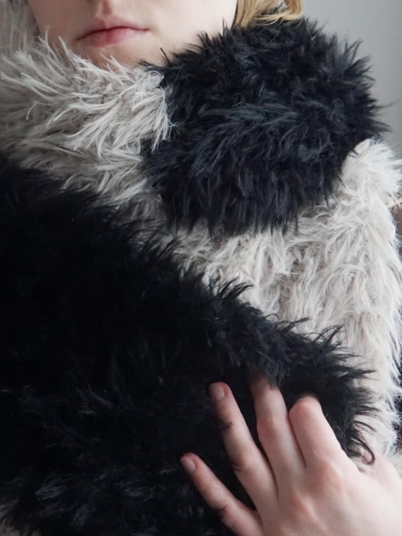May include: A long, plush scarf featuring a color-blocked design with alternating sections of deep black and light beige faux fur. The texture is shaggy and dense, providing a thick, layered appearance across the entire length of the accessory.