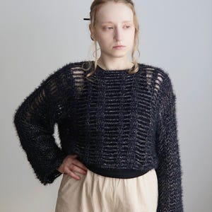 May include: A black fuzzy long-sleeve sweater with a horizontal ladder-stitch pattern and a wide crew neckline. The knit fabric has a textured, hairy appearance with subtle silver metallic threads woven throughout the dark yarn.