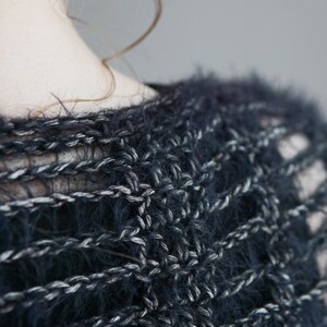 May include: A dark navy blue and silver metallic knit sweater featuring a loose, open-weave crochet pattern. The garment is crafted from a fuzzy, textured yarn that creates a soft, hairy appearance across the surface of the interlocking stitches.
