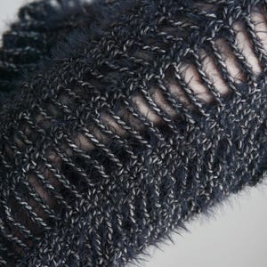 May include: A dark charcoal gray knit garment featuring a fuzzy, textured yarn composition. The piece displays a prominent open-work ladder stitch pattern, creating vertical gaps between the thick, interwoven strands of dark and light gray fibers.