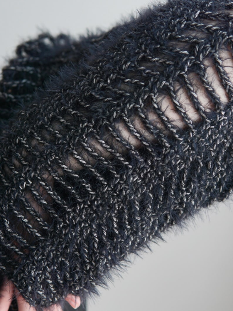 May include: A dark charcoal gray knit garment featuring a fuzzy, textured yarn composition. The piece displays a prominent open-work ladder stitch pattern, creating vertical gaps between the thick, interwoven strands of dark and light gray fibers.