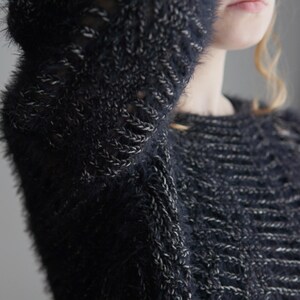 May include: A dark navy blue and silver fuzzy knit sweater featuring a textured, open-stitch pattern throughout the fabric. The garment has long sleeves and a round neckline, constructed from a soft, shaggy yarn with metallic silver accents.