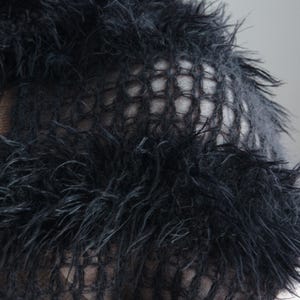 May include: A black knit garment featuring a textured, shaggy, faux-fur-like yarn interspersed with sections of an open, grid-like mesh pattern. The material has a long, wispy pile that creates a dense, layered appearance across the surface.