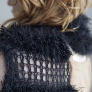 May include: A black knitted scarf featuring a combination of fuzzy, textured yarn sections and open, grid-like mesh panels. The accessory has a long, rectangular shape with a soft, shaggy appearance created by the loose fibers of the dark yarn.