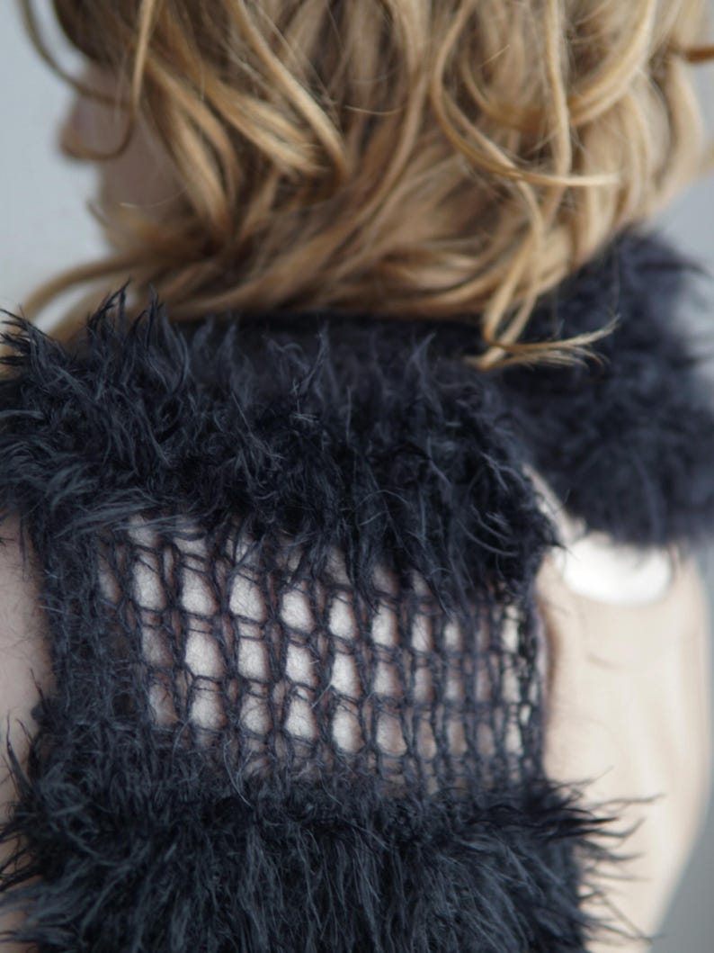 May include: A black knitted scarf featuring a combination of fuzzy, textured yarn sections and open, grid-like mesh panels. The accessory has a long, rectangular shape with a soft, shaggy appearance created by the loose fibers of the dark yarn.