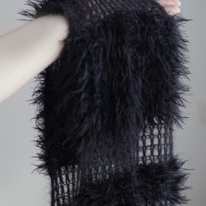 May include: A black scarf featuring a loose, open-knit mesh construction interspersed with thick, shaggy, faux-fur-like textured sections. The design consists of alternating rows of sheer, grid-like knitting and dense, fuzzy, elongated black fibers.