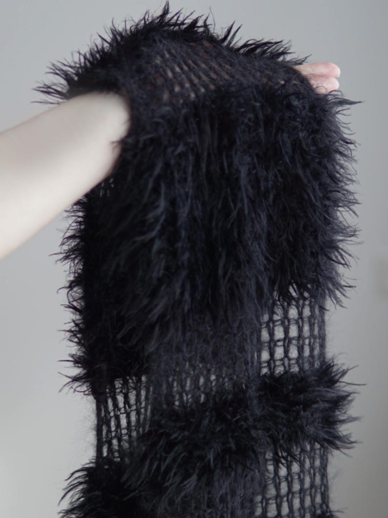 May include: A black scarf featuring a loose, open-knit mesh construction interspersed with thick, shaggy, faux-fur-like textured sections. The design consists of alternating rows of sheer, grid-like knitting and dense, fuzzy, elongated black fibers.