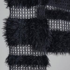 May include: A black textile featuring alternating horizontal bands of dense, shaggy, faux-fur-like fibers and open, grid-like mesh sections. The fabric displays a high-contrast texture with thick, fuzzy horizontal stripes separated by thin, transparent netting.