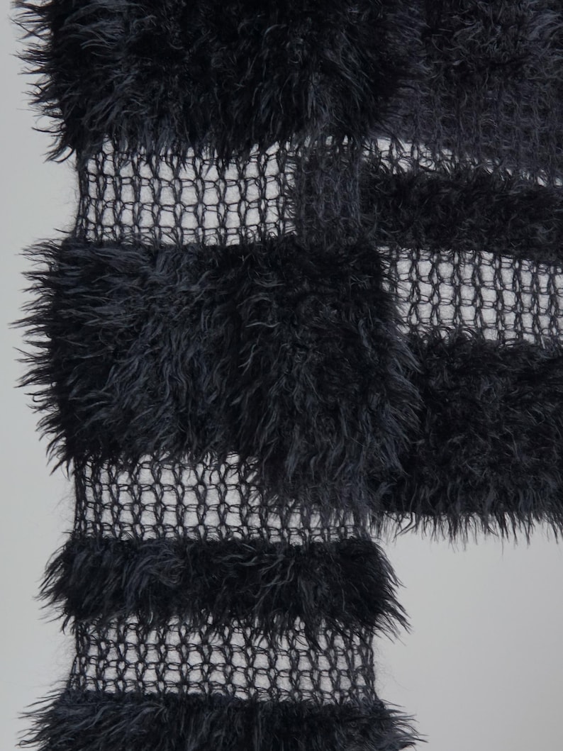 May include: A black textile featuring alternating horizontal bands of dense, shaggy, faux-fur-like fibers and open, grid-like mesh sections. The fabric displays a high-contrast texture with thick, fuzzy horizontal stripes separated by thin, transparent netting.