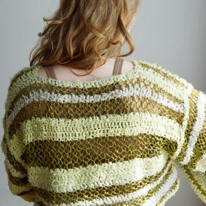 May include: A long-sleeve crochet jumper featuring horizontal stripes in shades of olive green, lime green, and white. The garment is constructed with a mix of solid textured yarn bands and openwork mesh sections, creating a varied, layered appearance.