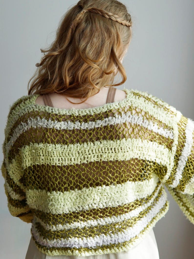 May include: A long-sleeve crochet jumper featuring horizontal stripes in shades of olive green, lime green, and white. The garment is constructed with a mix of solid textured yarn bands and openwork mesh sections, creating a varied, layered appearance.