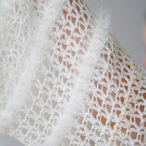 May include: A white open-knit garment featuring a delicate, semi-sheer crochet pattern with vertical stripes of fuzzy, textured yarn. The fabric displays a light, airy construction with a repeating diamond-shaped mesh design throughout the piece.