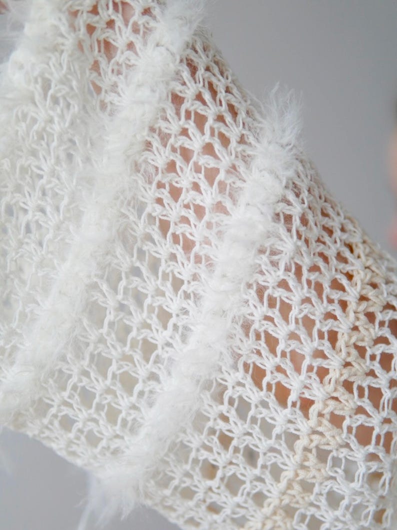 May include: A white open-knit garment featuring a delicate, semi-sheer crochet pattern with vertical stripes of fuzzy, textured yarn. The fabric displays a light, airy construction with a repeating diamond-shaped mesh design throughout the piece.