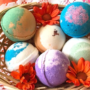 May include: A wicker basket filled with six colorful bath bombs, each with a unique swirl pattern. The bath bombs are surrounded by orange flowers.