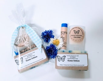 May include: A gift set of handmade soap and lotion bars with a clean cotton scent. The set includes a bar of soap, a lotion bar, and a lip balm. The products are packaged in a clear plastic bag with a blue and white checkered ribbon. The soap and lotion bars are labeled with the brand name "Ostars Organics Ltd" and the scent "Clean Cotton".
