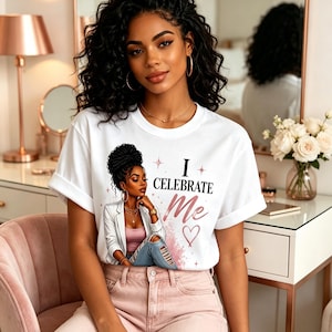 May include: A white short-sleeved t-shirt featuring a graphic illustration of a person with dark curly hair wearing a white blazer and blue jeans. The text "I CELEBRATE Me" is printed in black and pink, accompanied by a pink heart and star accents.