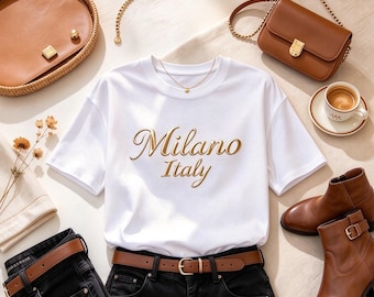 May include: A white short-sleeved t-shirt with the gold text Milano Italy printed on the front, paired with black jeans, a brown leather belt, brown leather ankle boots, a small brown shoulder bag with a gold chain, and a round brown bag.