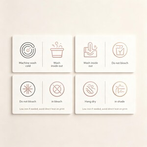 May include: A set of four white rectangular care instruction cards featuring rose gold line art icons and text. The cards display symbols and instructions for machine wash cold, wash inside out, do not bleach, hang dry in shade, and low iron.