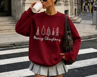 May include: A deep red long-sleeve crewneck sweatshirt featuring a white graphic print of five stylized Christmas trees and the text Merry Christmas in a cursive script font across the center of the chest.