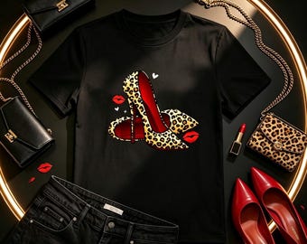 May include: A black short-sleeved t-shirt featuring a graphic print of leopard-print high-heeled shoes with red soles, surrounded by small red lip icons and white hearts. The shirt is displayed alongside black handbags, a leopard-print wallet, and red pumps.