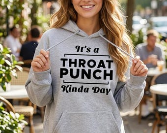 May include: A light gray hooded sweatshirt featuring a front kangaroo pocket and long sleeves. The chest displays black text that reads: It's a THROAT PUNCH Kinda Day, with the words enclosed in a simple black rectangular frame.
