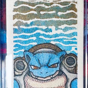 May include: A rectangular trading card featuring a detailed illustration of a blue, turtle-like creature with two large cannons on its back. The background consists of horizontal wavy lines in shades of blue and gold, encased in a clear plastic holder.