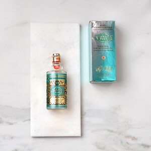 May include: A bottle of 4711 Original Eau de Cologne with a gold and teal label and a matching box. The bottle is on a white marble surface. The text on the bottle and box is in German and English.