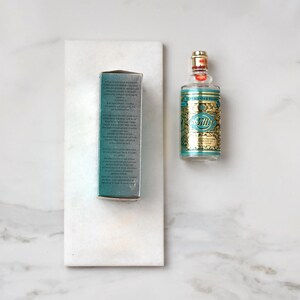 May include: A bottle of 4711 Eau de Cologne with a teal and gold label, and a matching box. The bottle has a gold cap and a red seal. The box is teal with white text.