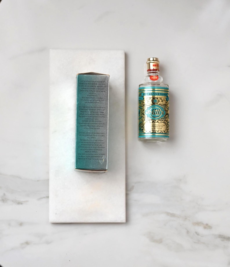 May include: A bottle of 4711 Eau de Cologne with a teal and gold label, and a matching box. The bottle has a gold cap and a red seal. The box is teal with white text.