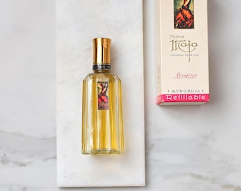 May include: A vintage perfume bottle with a gold cap and a rectangular shape, filled with a yellow liquid. The bottle sits on a white marble surface next to a matching box with the text "Nueva Maja" and "Atomizer."