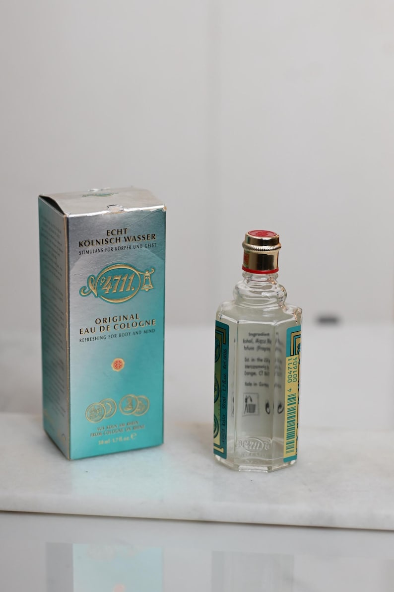 May include: A vintage bottle of 4711 Original Eau de Cologne with its original box. The box is silver and teal with gold accents. The cologne bottle is clear with a red and gold cap. The text "4711" is visible on both the box and the bottle.