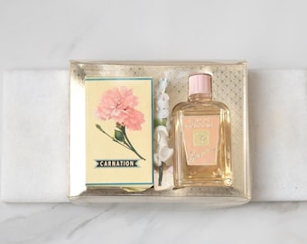 May include: A vintage perfume set in a clear box. The set includes a small perfume bottle with a pink cap and a box with a carnation illustration and the word "CARNATION". The box has a gold pattern.