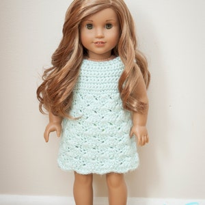 May include: A doll wearing a light blue crocheted dress. The doll has long, wavy, light brown hair and blue eyes.