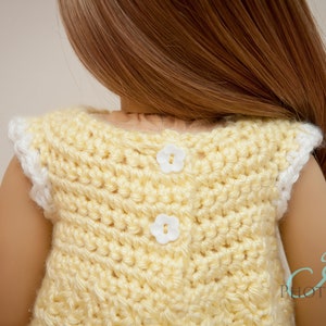 Op de afbeelding: Een gele, gebreide, mouwloze jurk met witte bies en twee witte, bloemvormige knopen op de rug.