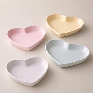 Może przedstawiać: Cztery ceramiczne talerze w kształcie serca w pastelowych kolorach: różowym, żółtym, jasnoniebieskim i białym. Każdy talerz ma obramowanie z koralików. Idealne do serwowania przystawek lub deserów, te talerze dodają uroku.