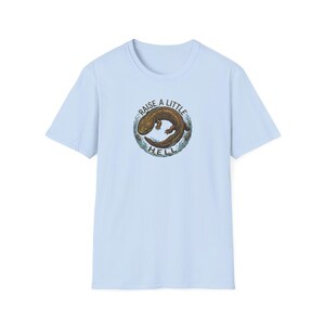 May include: Pale blue t-shirt with a circular graphic. The graphic shows a brown salamander and the text "RAISE A LITTLE HELL". The design is centered on the front of the short-sleeved shirt.