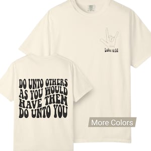 Könnte beinhalten: Zwei cremefarbene T-Shirts. Eines zeigt den schwarzen Text "DO UNTO OTHERS AS YOU WOULD HAVE THEM DO UNTO YOU". Das andere hat eine Handgeste und den schwarzen Text "Luke 6:31".