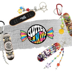 May include: Four miniature skateboard keychains featuring diverse graphic designs, including a black Tech Deck, a Rowley Flip board, a panda tie-dye board, and a graphic board. Each keychain includes metal rings, colorful beads, star charms, and spikes.