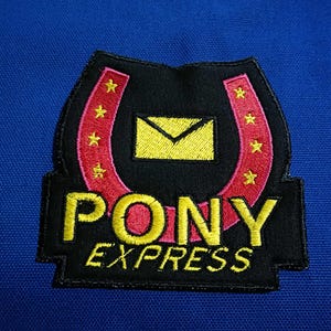 May include: Embroidered patch with the words "PONY EXPRESS" in yellow, set against a black background with a red horseshoe design. The patch includes a yellow envelope and gold stars, on a blue background.