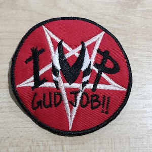 Puede incluir: Un parche redondo rojo con borde negro. Presenta un pentagrama blanco, cuernos negros y el texto "IMP GUD JOB!!" en negro. El diseño probablemente está bordado en el parche.