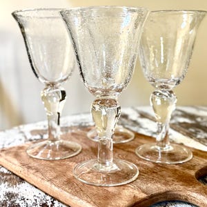 May include: Three clear glass goblets with a distinct seeded texture throughout the bowls. Each goblet features a smooth, rounded stem and a wide, flat circular base. The glass has a slightly irregular, hand-blown appearance with visible air bubbles.