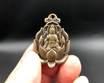 Peut inclure: Un pendentif en métal de couleur bronze présentant une sculpture en relief d'une figure assise au centre d'un motif de fleur de lotus stylisée. Le pendentif possède une petite boucle circulaire au sommet et une finition patinée sombre.
