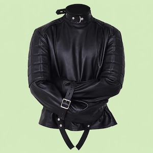 May include: A black long-sleeved garment featuring a high collar with a metal buckle, quilted shoulder panels, and long sleeves that cross over the front. The piece includes adjustable leather-like straps with metal buckles and silver-toned rivets.