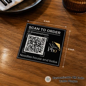 May include: A square black table plaque measuring 4 inches by 4 inches with white text that reads SCAN TO ORDER, @nonamephopdx, and Noodles house and boba. It features a central QR code and a gold logo with the text No Name Pho.