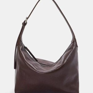 May include: A dark brown shoulder bag with a curved shape and a long strap. The bag has a zipper closure and a shiny, leather-like texture. The strap is adjustable with a silver-colored buckle.