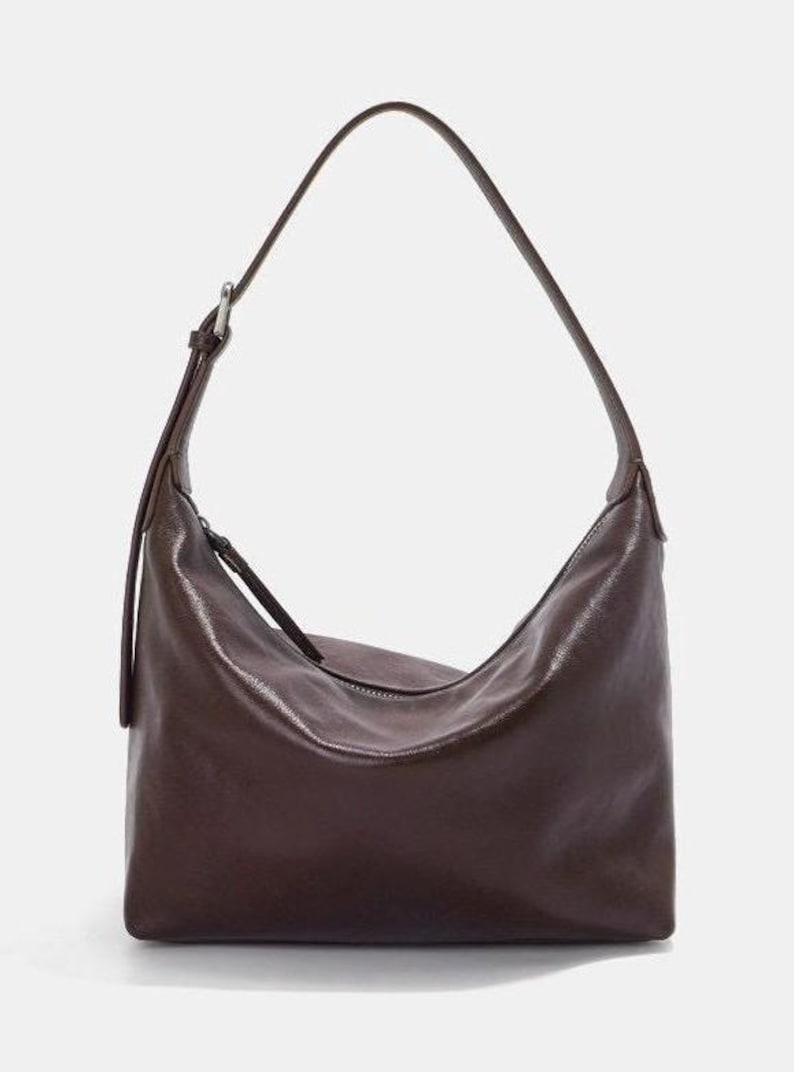 May include: A dark brown shoulder bag with a curved shape and a long strap. The bag has a zipper closure and a shiny, leather-like texture. The strap is adjustable with a silver-colored buckle.