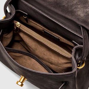 May include: Open view of a dark brown leather handbag with a flap closure. The interior features a zippered pocket and multiple compartments. Gold-toned hardware accents the bag, including the clasp and handle attachments.