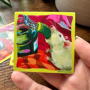 May include: Square sticker with a yellow border featuring a cartoon illustration of a white rat eating a pickle from a jar. The background includes red, pink, and orange colors. The sticker has the text "@6avenue.studio".