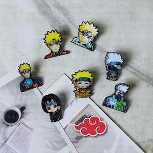 May include: A collection of colorful enamel pins featuring characters from the anime series Naruto. The pins depict various characters with spiky yellow hair, blue eyes, and other distinctive features. A red cloud pin is also included.