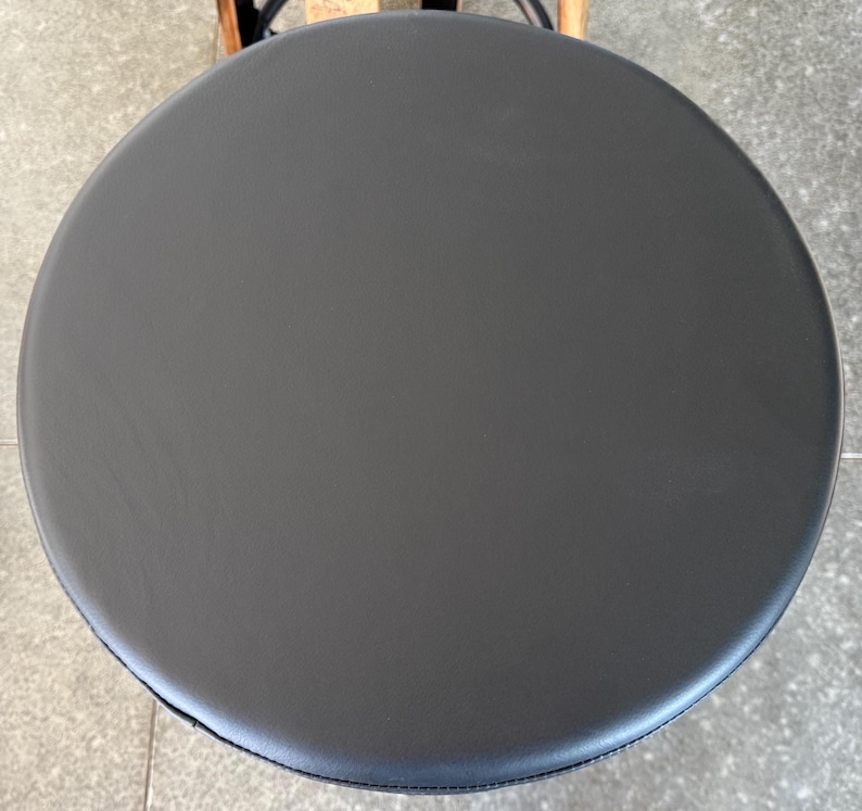 May include: A circular stool seat featuring a smooth, matte black surface. The top is perfectly round with a clean, uniform finish, showing no visible textures or patterns. The edges are slightly rounded, creating a simple, functional design.